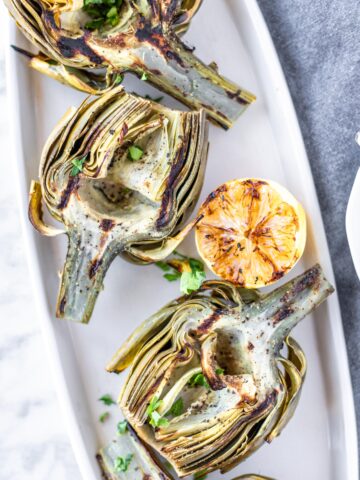 Delicious grilled artichokes with a zesty lemon garlic dipping sauce. A beautiful artichoke appetizer or side dish. #athousandcrumbs #grilled #artichokes #lemongarlic #dippingsauce